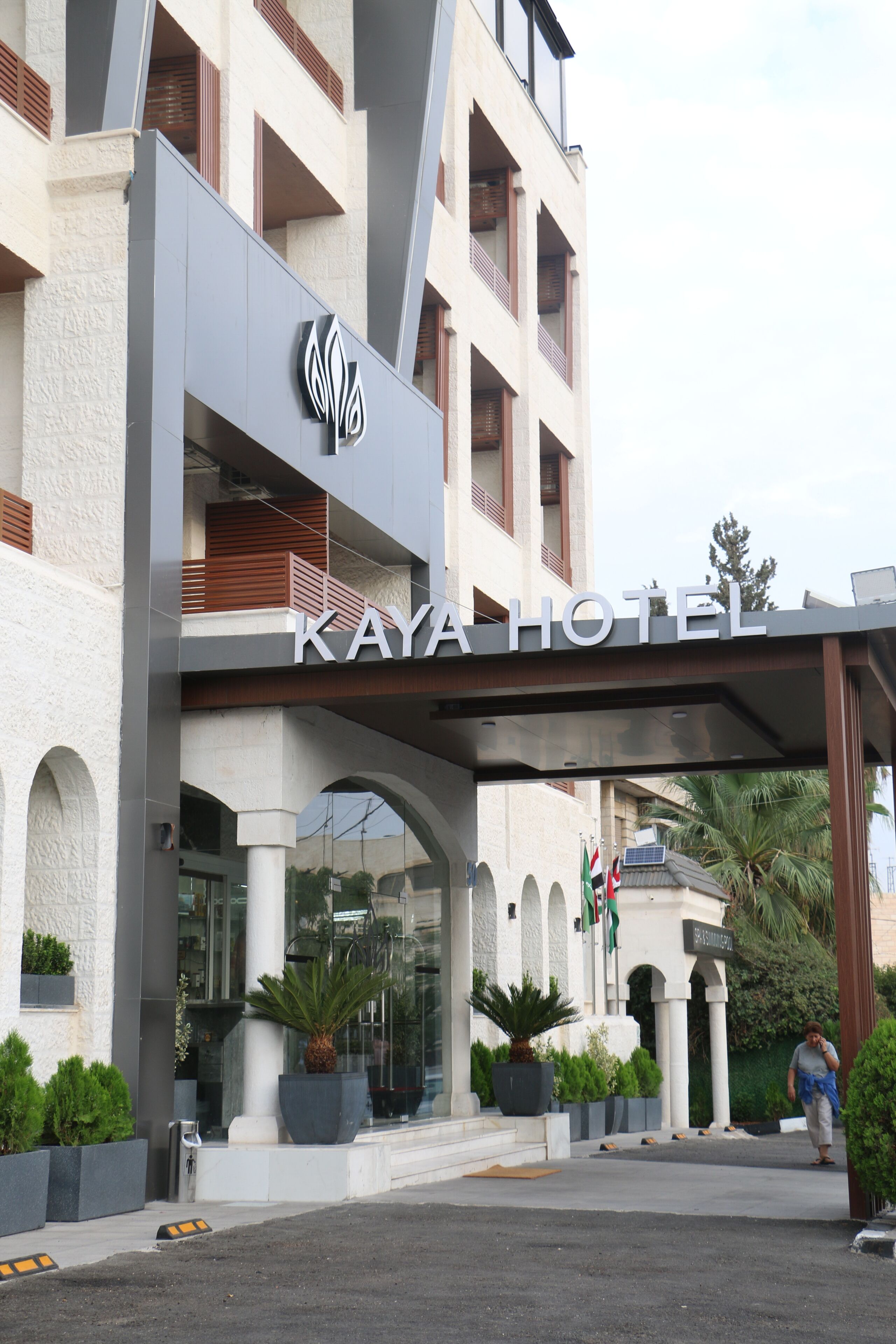 L’extérieur de l’hôtel Kaya présente une architecture moderne, avec une entrée imposante, de grands pots de plantes et un drapeau bien visible.