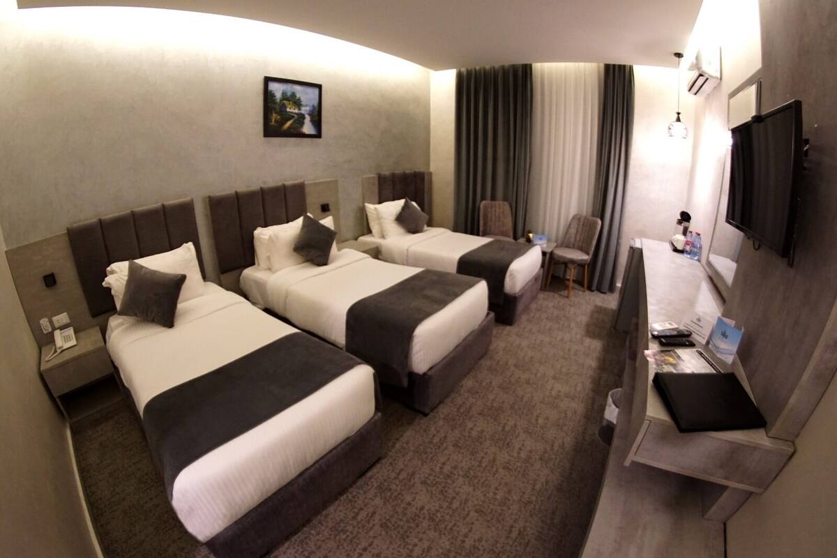 A hotel room with two beds, a desk, a chair, a TV, and a painting on the wall.