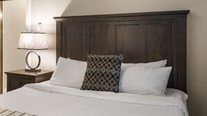 A neatly made bed with white linens, a dark wooden headboard, and a patterned pillow.