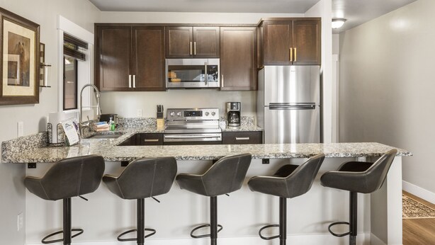 A modern kitchen with dark wooden cabinets, stainless steel appliances, a granite countertop, and four bar stools.