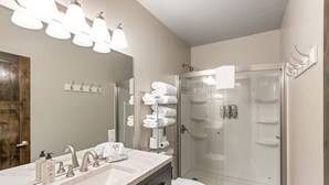A modern bathroom with a large mirror, a sink with two faucets, a toilet, and a glass-enclosed shower.