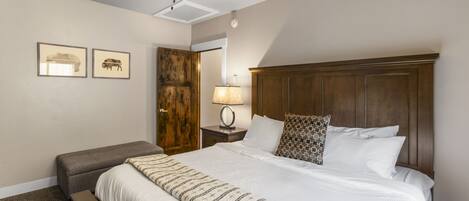 Ein ordentlich eingerichtetes Schlafzimmer mit einem großen Bett, einem Holz-Kopfstück, einem Nachttisch mit Lampe und zwei gerahmten Bildern an der Wand.