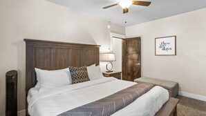 Une chambre d’hôtel avec un grand lit, un ventilateur de plafond, une lampe de chevet, un banc et une citation encadrée au mur.