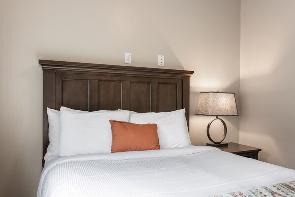 A neatly made bed with white and orange pillows, a wooden headboard, and a bedside table with a lamp.