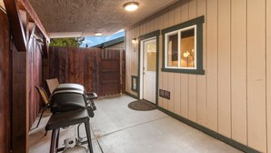 A covered outdoor area with a grill, chairs, and a door leading to a building.