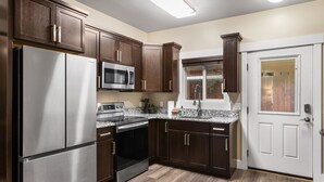 A modern kitchen with stainless steel appliances, dark wood cabinets, and a white door.
