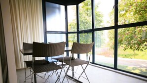 Una habitación con un ventanal amplio, dos sillas de mimbre y una mesa.