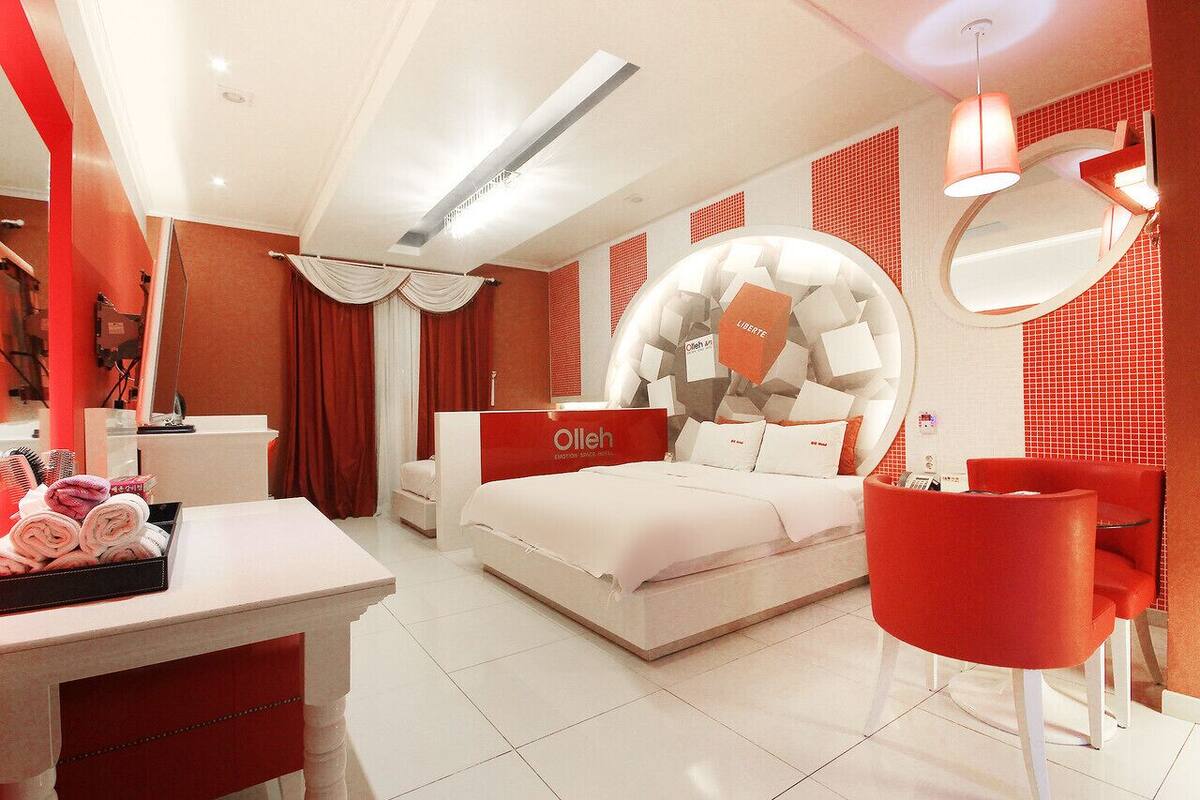 Une chambre d’hôtel moderne avec un lit, un bureau avec des serviettes et une chaise rouge.