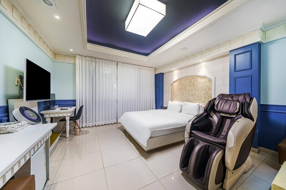 Une chambre d’hôtel équipée d’un lit, d’un fauteuil massant, d’un bureau avec un ordinateur et d’une télévision.