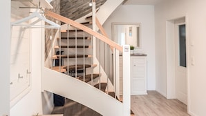 Una escalera moderna con barandilla de madera y balaustradas de metal, que conduce a una plataforma con un armario blanco y una pequeña planta en maceta.