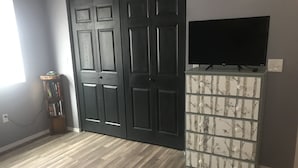 Une pièce avec un plancher en bois, une porte noire, un téléviseur posé sur un meuble et une bibliothèque.