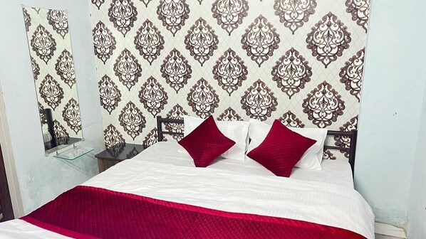 A neatly made bed with a white and red bedspread, two red pillows, and a patterned wallpaper. - Vrindavan Hotel (Mathura)