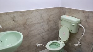 Un baño con inodoro y lavamanos verdes, y un cubo azul.