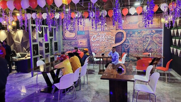 Una cafetería con mesas y sillas, decorada con globos y flores colgantes.
