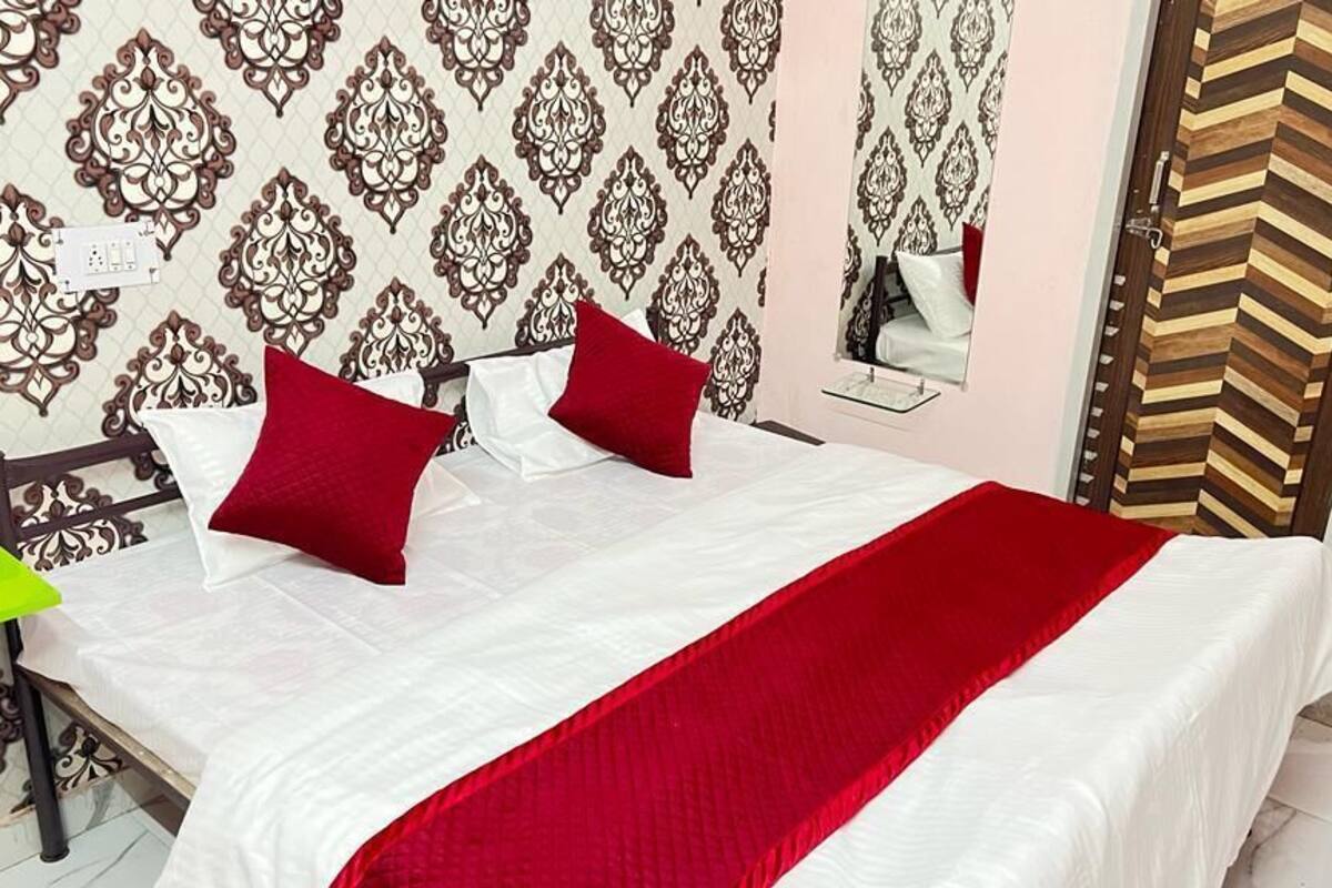 Un lit bien fait, avec une literie blanche et rouge, un papier peint à motifs et un miroir au mur.