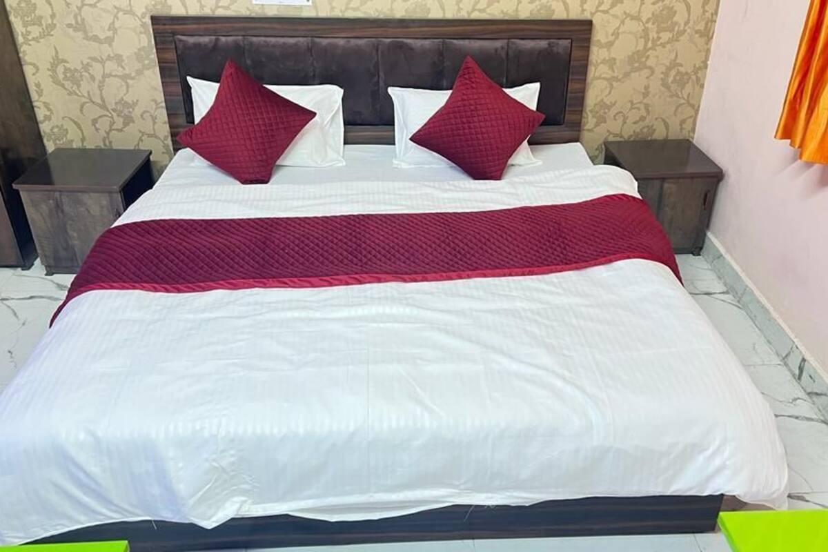 Un lit bien fait, avec une couverture blanche et rouge, deux oreillers et une tête de lit en bois.
