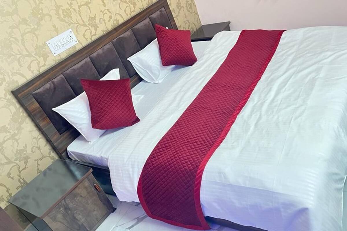 Un lit bien fait, recouvert d’une couvre-lit blanche et rouge, avec deux oreillers rouges et une tête de lit en bois.