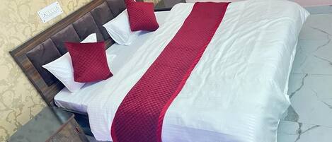 Una cama bien hecha con una colcha blanca y roja, dos almohadas rojas y un cabecero de madera.