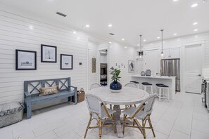 Een moderne keuken met witte kasten, een roestvrijstalen koelkast, en een eethoek met een ronde tafel en rieten stoelen.