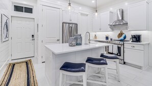 Una cucina moderna con mobili bianchi, elettrodomestici in acciaio inossidabile e un'isola centrale con sgabelli da bar.