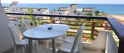 A balcony with a table and chairs, overlooking a beach and residential buildings.