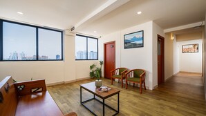 A spacious living area with a wooden floor, a sofa, a coffee table, and two chairs. Large windows offer a view of the cityscape. - C J Grande Business Hotel (Kanayannur)