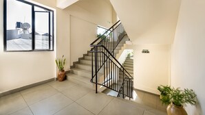 A modern hotel lobby with a staircase, a large window with a view of the city, and potted plants. - C J Grande Business Hotel (Kanayannur)