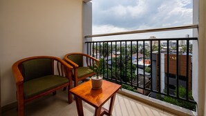 A balcony with two wooden chairs, a small table, and a potted plant. - C J Grande Business Hotel (Kanayannur)