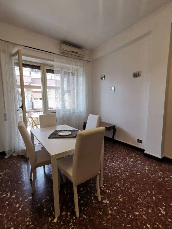 A dining area with a table and chairs, a window with curtains, and a terrazzo floor. - Sara's Apartment (Roma)