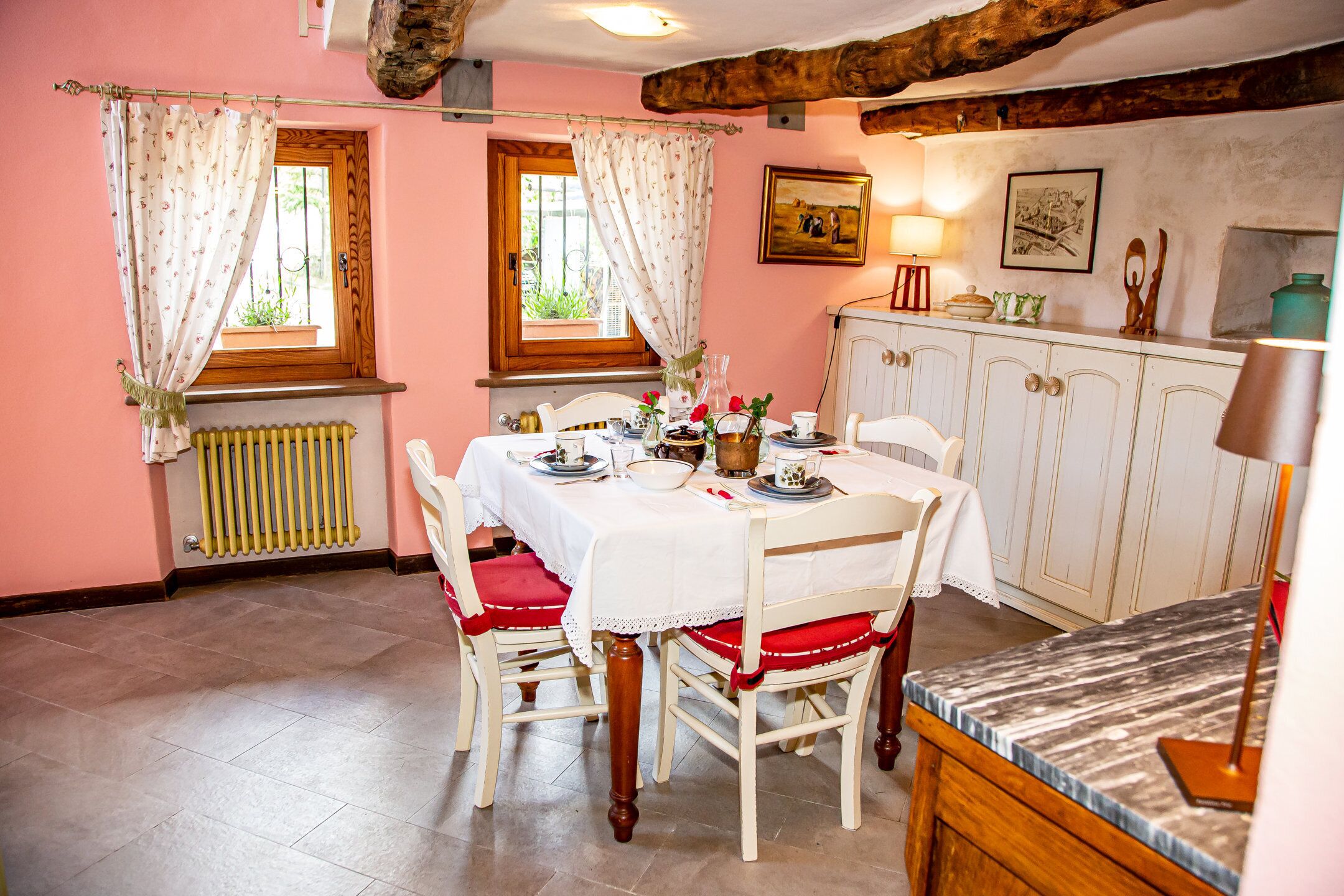 Ein Essbereich mit einem Tisch für vier Personen, weißen Stühlen mit roten Kissen, einer Holzschrank und einer Heizung.