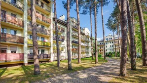 A multi-story residential building with balconies, surrounded by tall trees and a paved pathway. - Apartamenty Sun & Snow Morskie Oko (Miedzyzdroje)