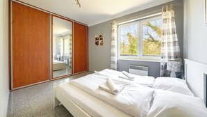 A bedroom with a large mirror, a bed with white linens, a radiator, and a window with curtains. - Apartamenty Sun & Snow Morskie Oko (Miedzyzdroje)