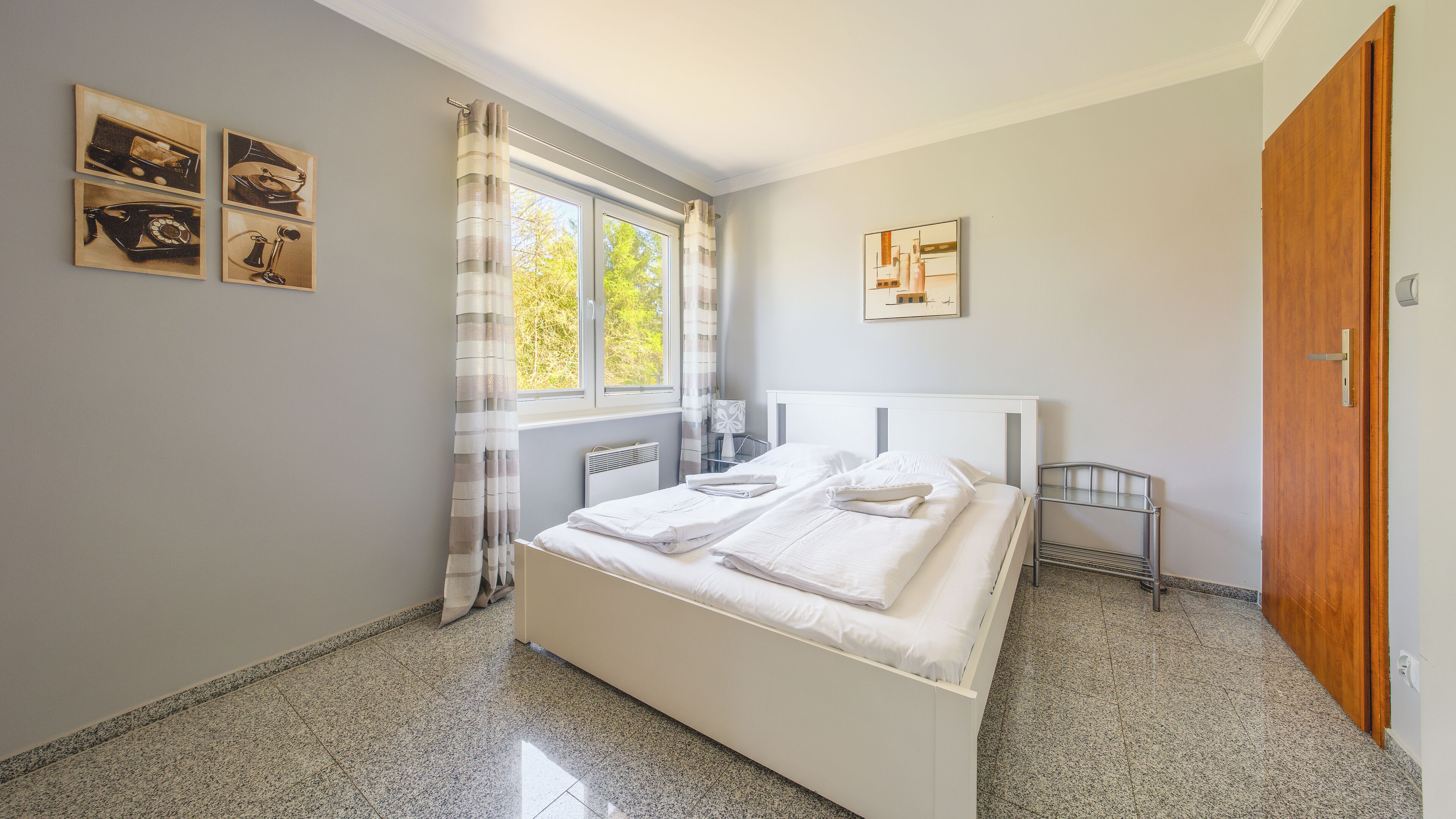 A bedroom with a bed, a window with curtains, a radiator, and a wooden door.