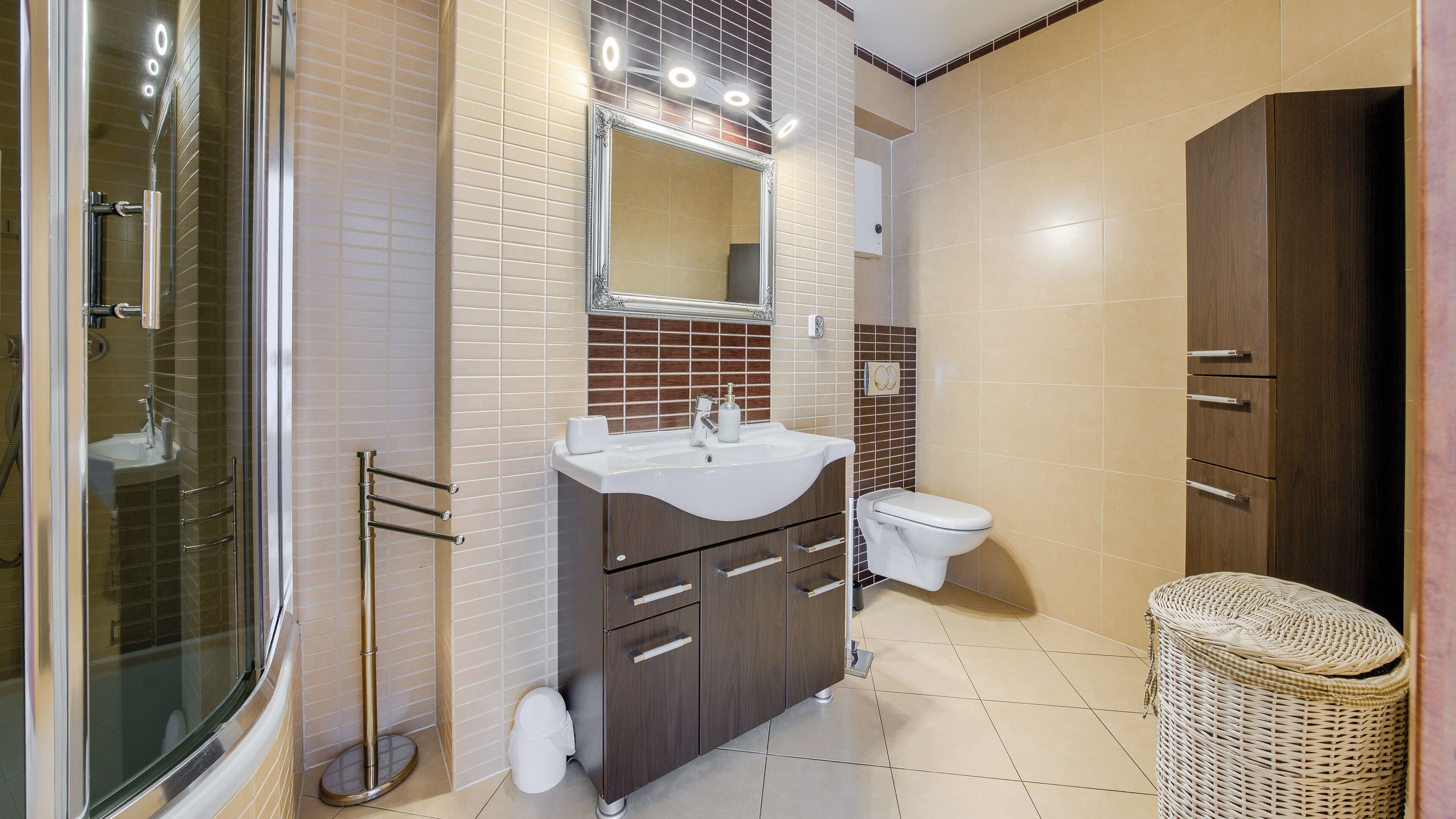 Un baño moderno con cabina de ducha de vidrio, tocador con espejo, inodoro y una cesta de mimbre.