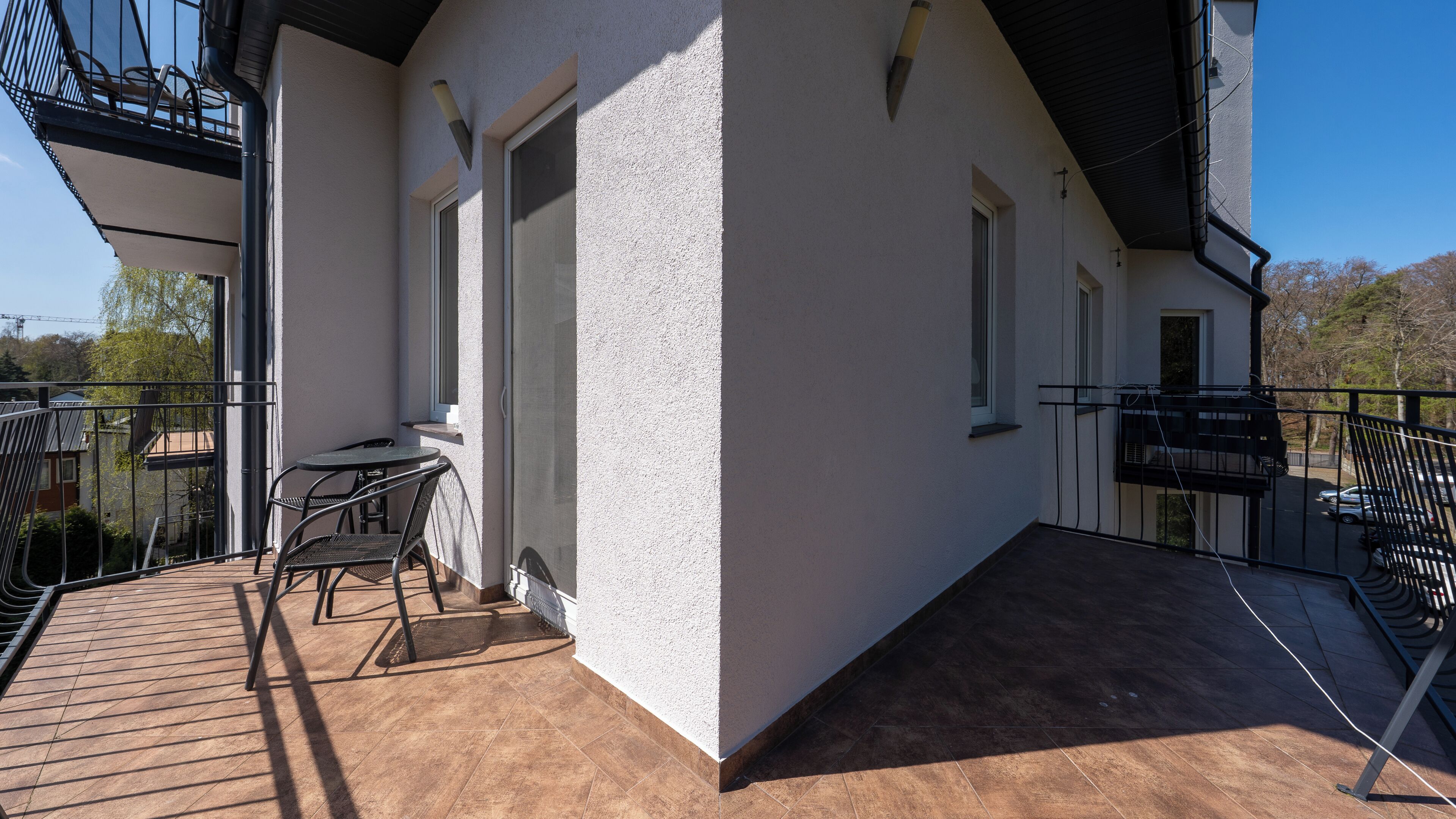 A balcony with a table and chairs, a white building, and a clear sky.