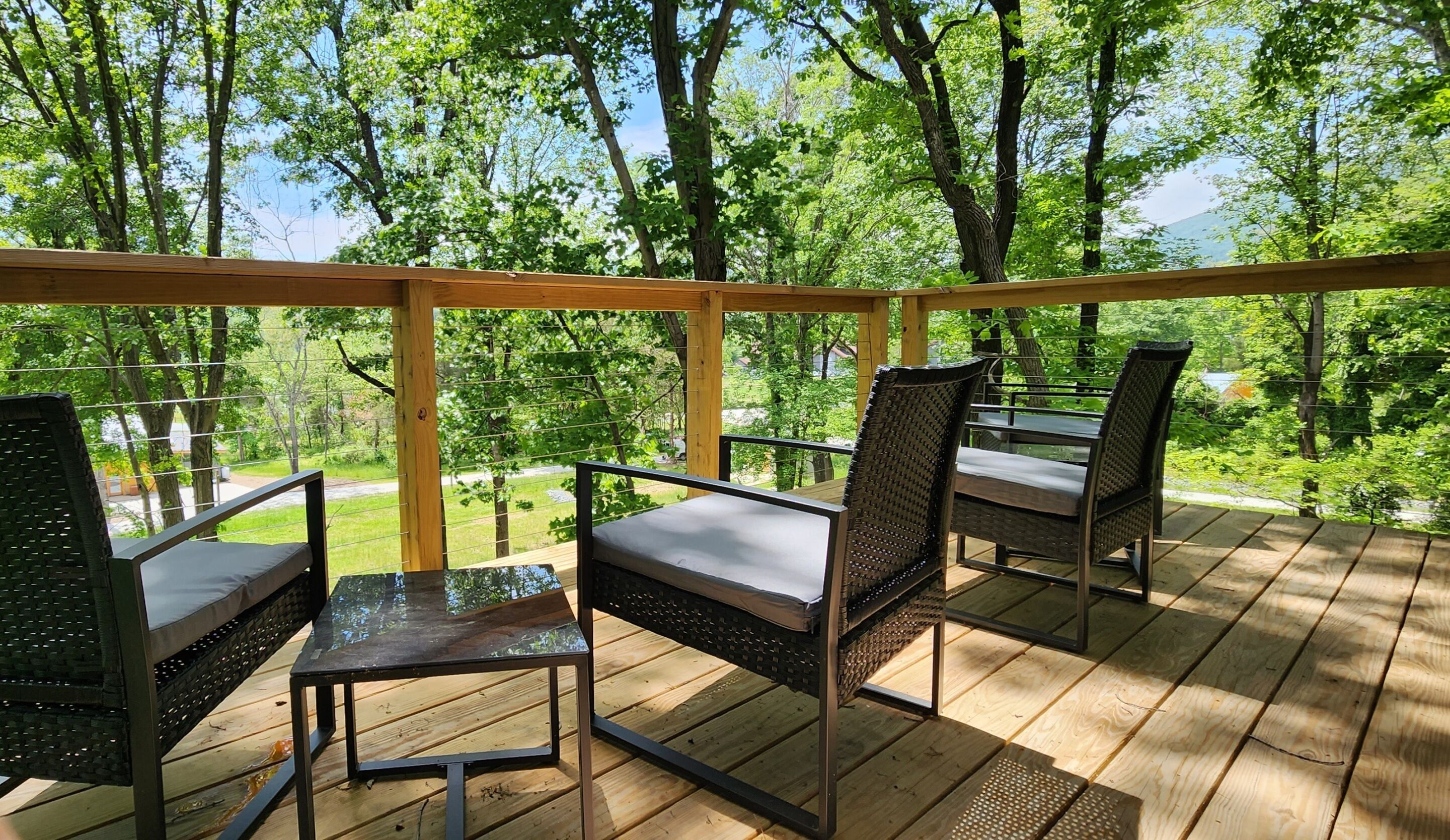 A wooden deck with outdoor furniture, including chairs and a table, overlooking a lush green landscape.