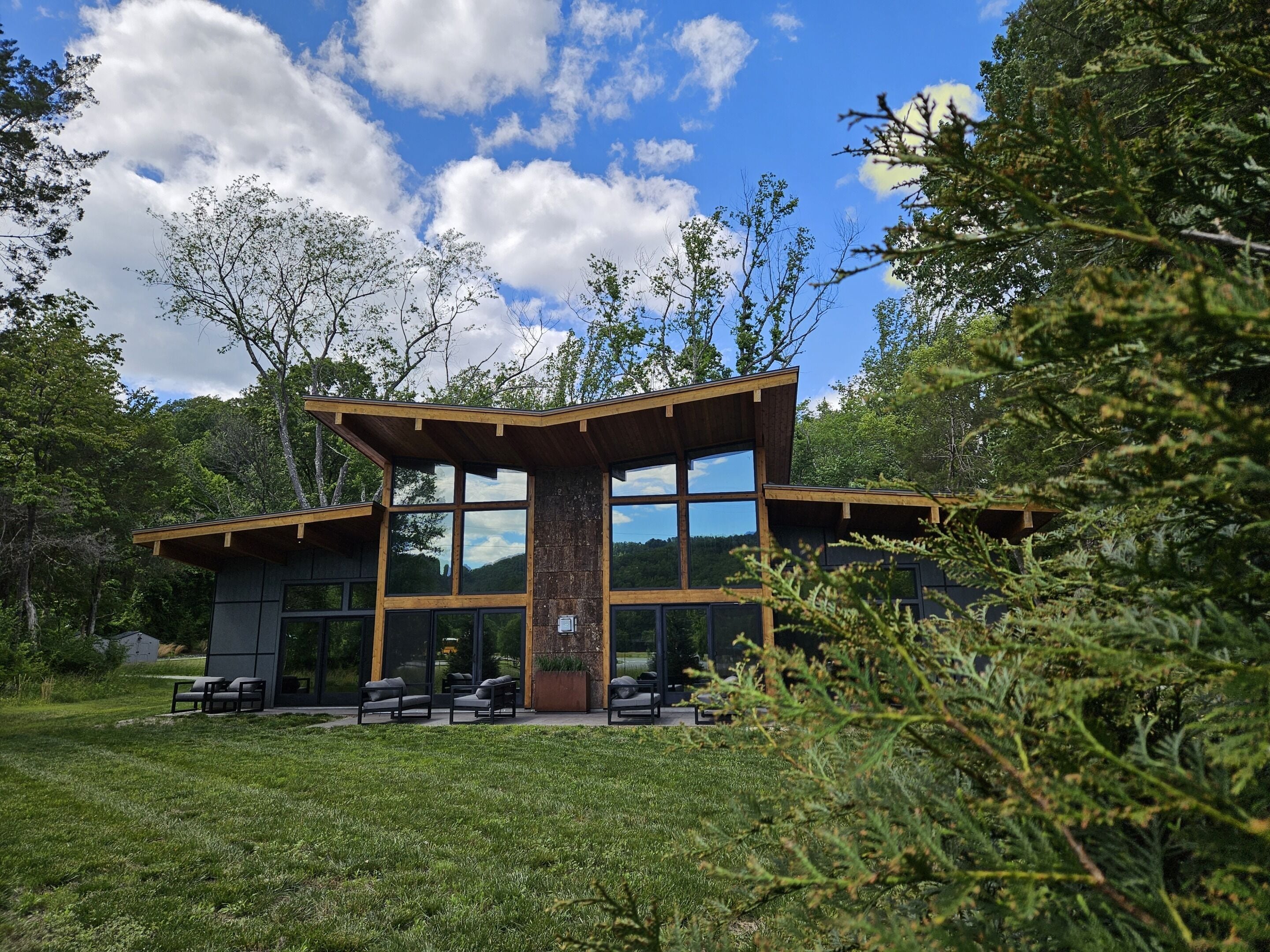 Ein modernes Gebäude mit großen Fenstern, Holzfassade und einem Rasenbereich mit Außenbestuhlung.