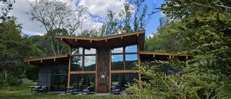 Ein modernes Gebäude mit großen Fenstern, Holzfassade und einem Rasenbereich mit Außenbestuhlung.