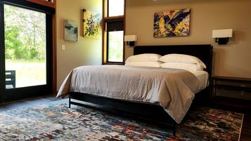 A bedroom with a bed, a patterned rug, artwork on the walls, and a view through the window.