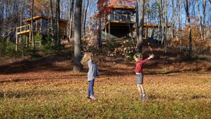 Une cabane dotée d’une terrasse en bois et d’une véranda en verre, entourée d’arbres et de feuilles d’automne.