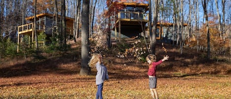 A cabin with a wooden deck and a glass enclosure, surrounded by trees and autumn leaves.