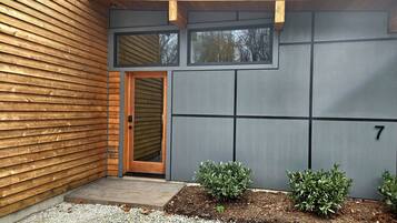 A modern building with a wooden exterior, a grey wall with a number '7', and a small garden area with gravel and plants.