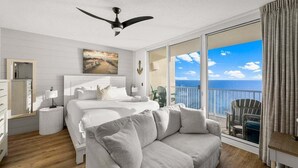 Une chambre d’hôtel dotée d’un grand lit, d’un canapé, d’un ventilateur de plafond, offrant une vue sur l’océan et disposant d’un balcon avec des sièges extérieurs.