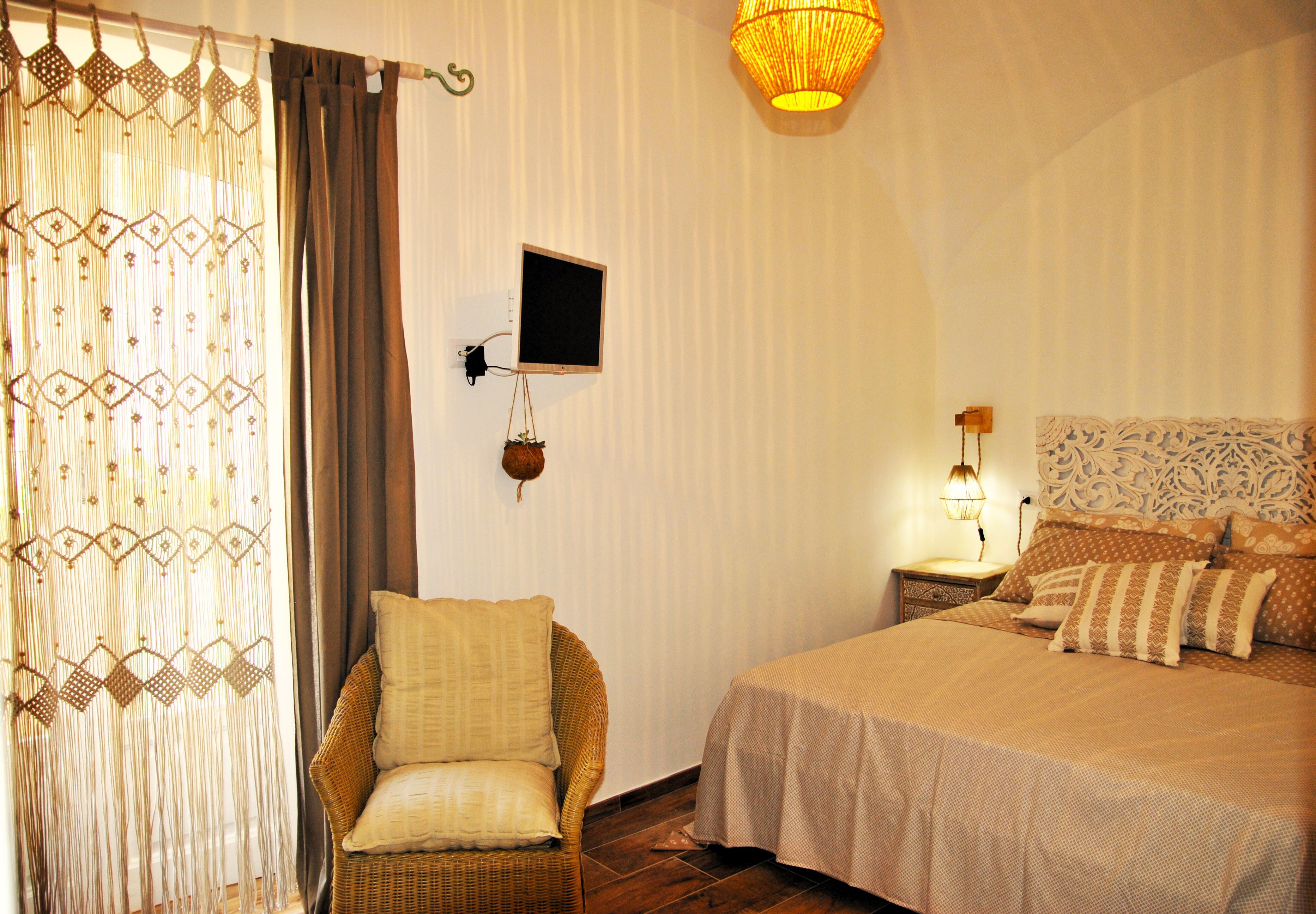 Een slaapkamer met een bed, een stoel, een aan de muur bevestigde televisie en een hanglamp.