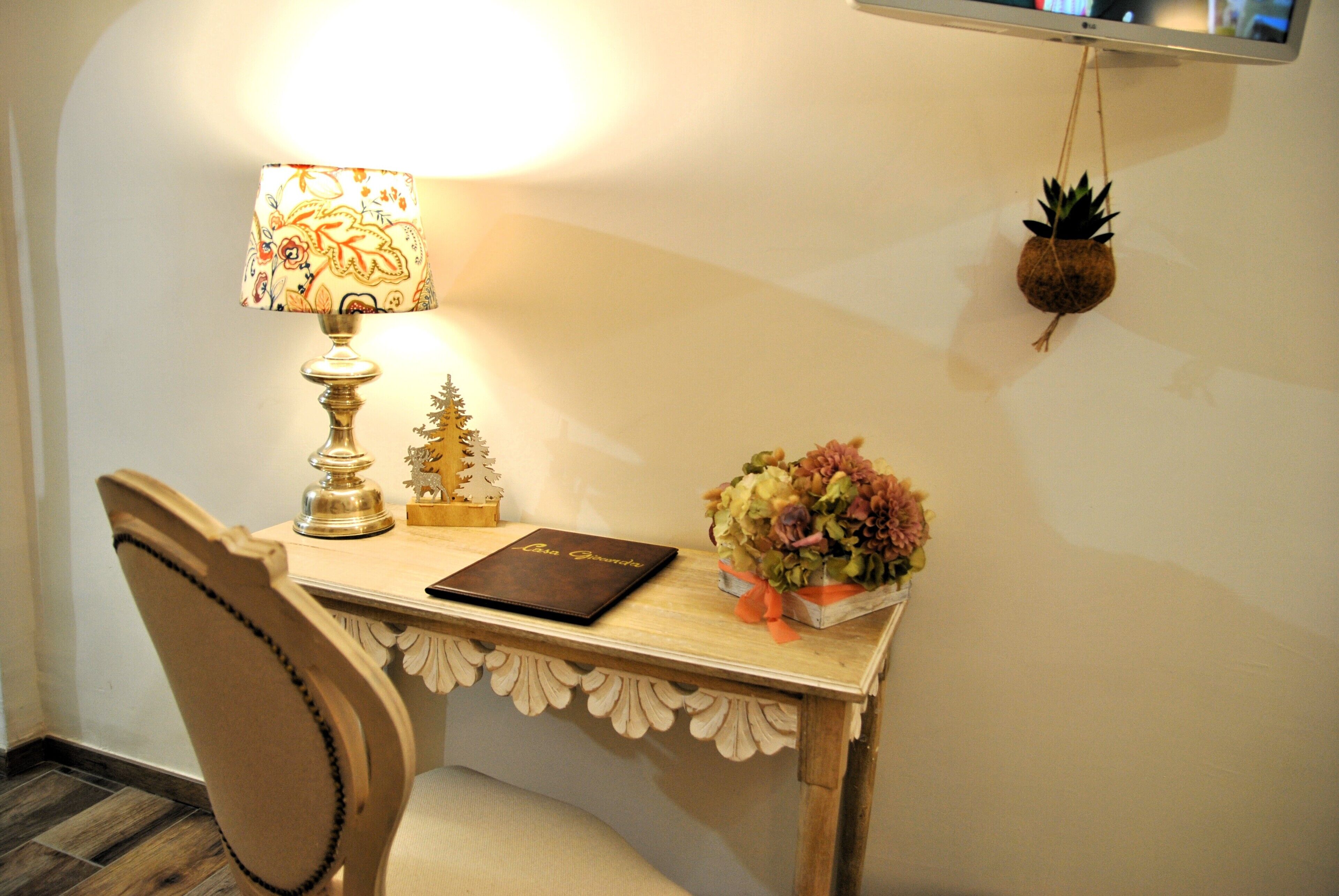 A desk with a lamp, a small Christmas tree, a book, and a flower arrangement.