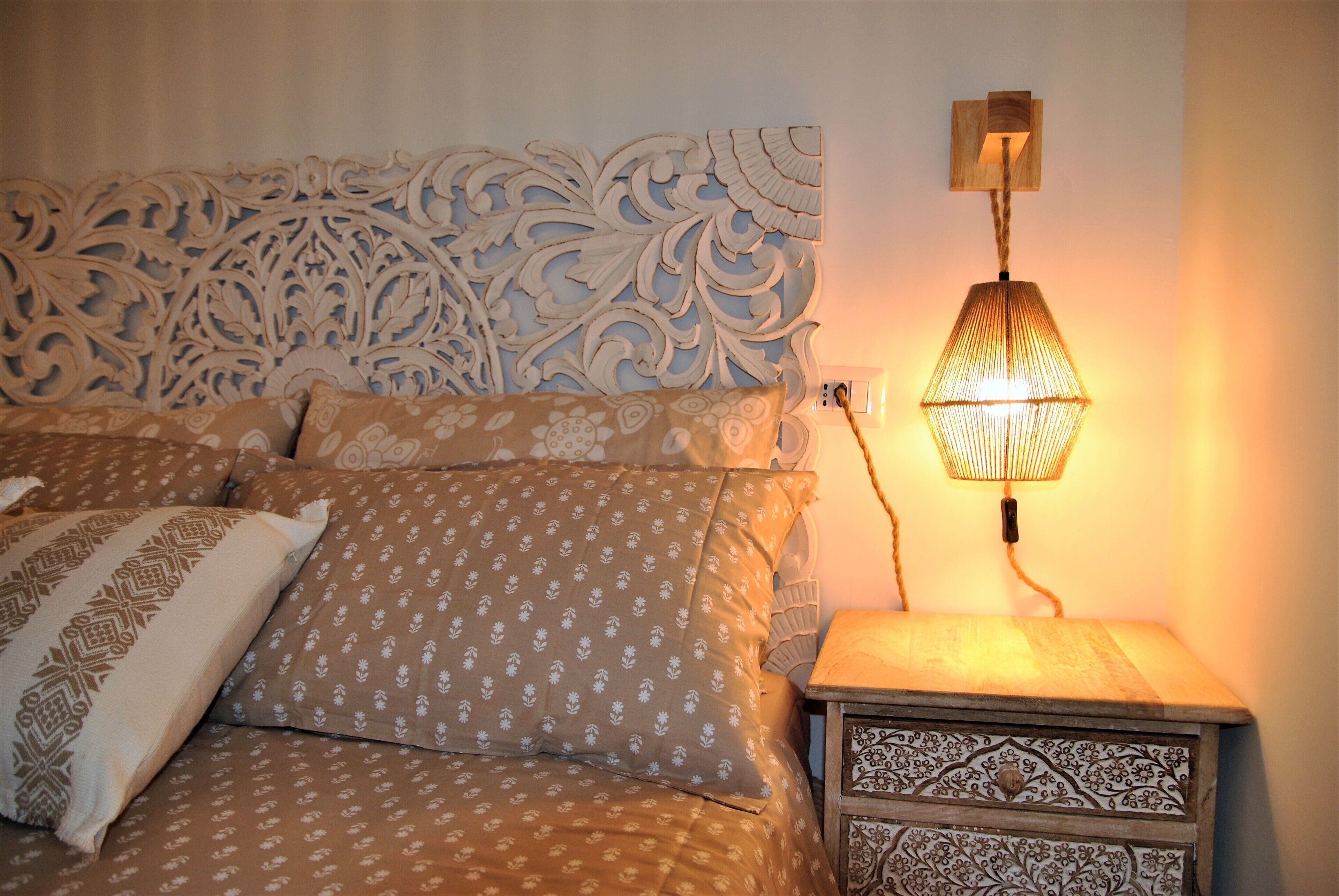 Un lit avec une literie à motifs, une tête de lit décorative et une lampe fixée au mur.