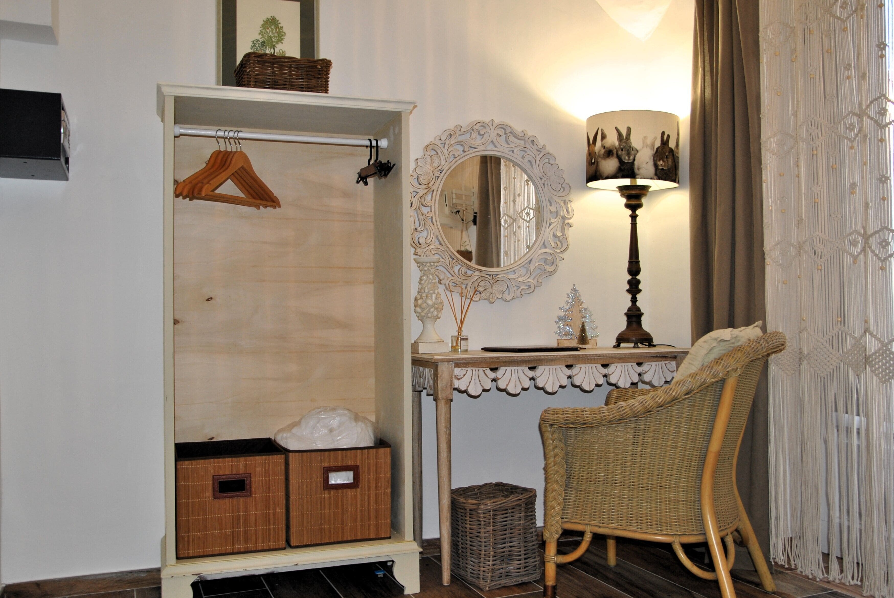Una habitación con un armario de madera, una silla de mimbre, un espejo y una lámpara.