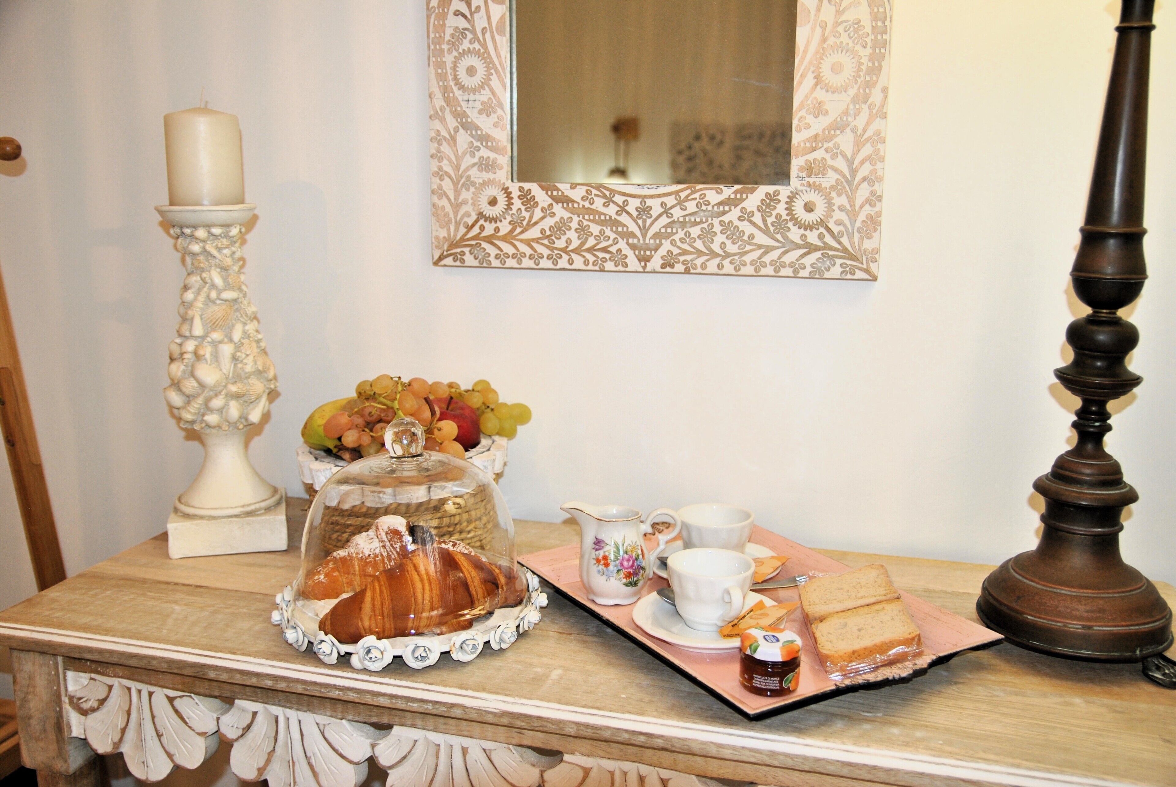 Une table de petit-déjeuner avec un croissant, un cloche en verre, un pichet, des tasses et un plateau contenant des sandwichs et de la confiture.