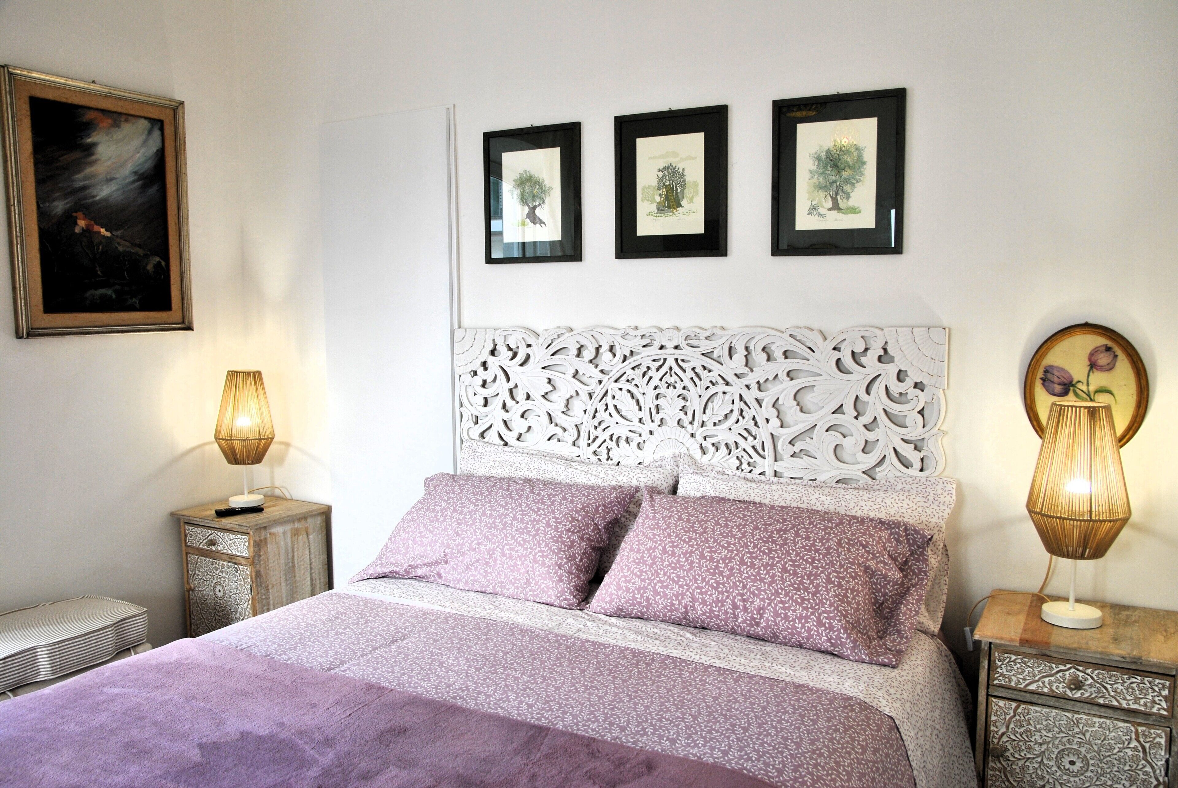 Un dormitorio ordenado con una cama, dos mesitas de noche y tres cuadros en la pared.
