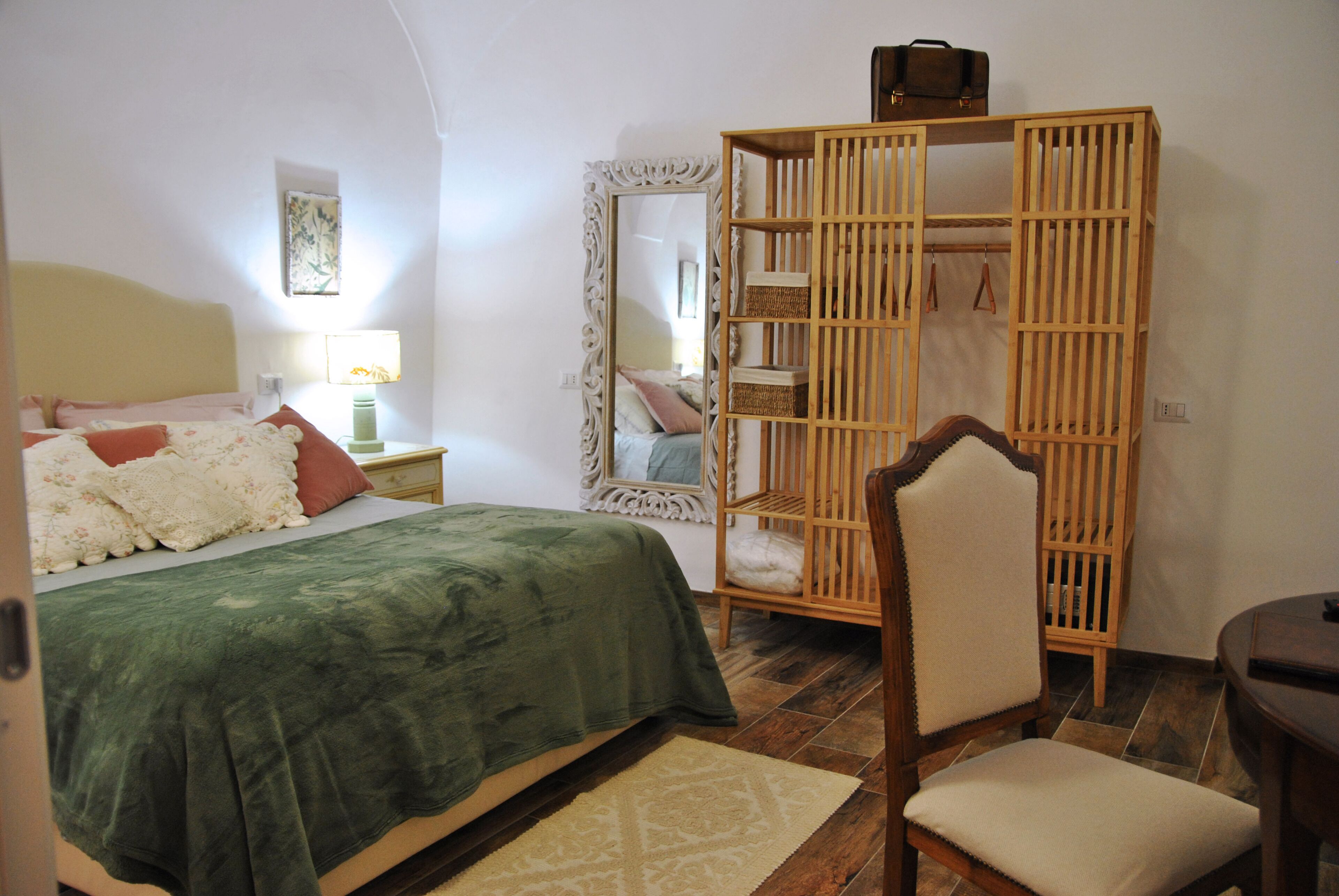 Un dormitorio con cama, una silla, armario y espejo.